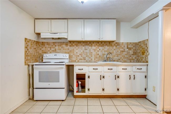 2nd unit Kitchen featuring white range with electric stovetop, white cabinetry, light tile patterned floors, sink, and decorative backsplash | Image 33