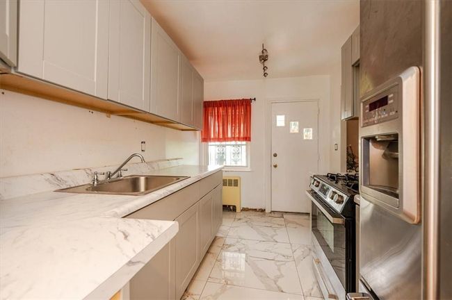 Kitchen featuring sink, stainless steel stove, radiator, light tile patterned floors, and refrigerator | Image 5