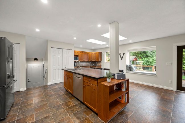 Kitchen featuring a sink, dark countertops, brown cabinets, stainless steel appliances, and a skylight | Image 16