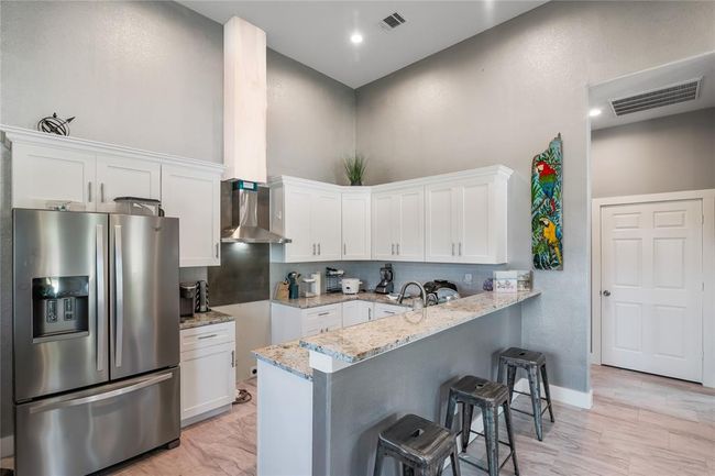 Modern kitchen featuring sleek stainless steel appliances, elegant white cabinetry, and a spacious granite countertop with seating—perfect for cooking and entertaining. | Image 4
