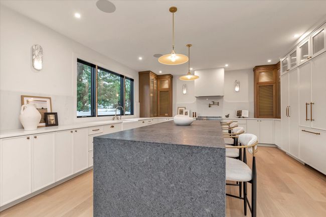 Kitchen featuring a breakfast bar, glass insert cabinets, light wood-style floors, a center island, and white cabinetry | Image 8