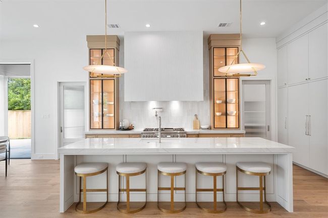 This kitchen features exquisite custom cabinetry with elegant glass doors, showcasing fine craftsmanship and attention to detail. Under-cabinet lighting highlights the shelves, creating a warm, inviting glow that beautifully accents the display items inside. | Image 16