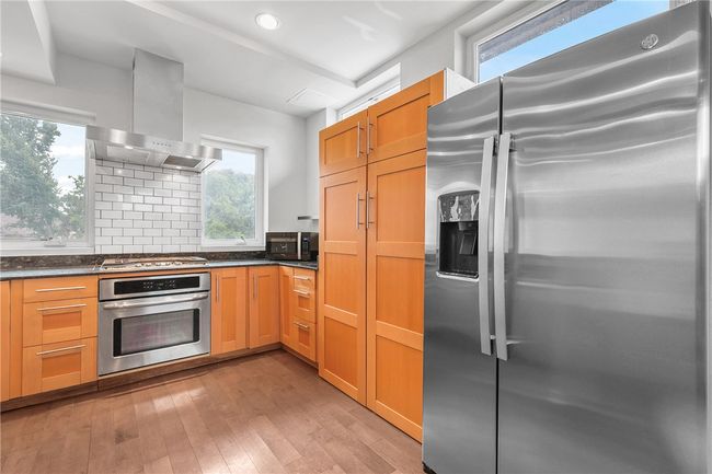 Kitchen featuring appliances with stainless steel finishes, wall chimney range hood, dark countertops, light wood-style floors, and plenty of natural light | Image 6