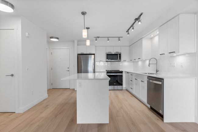 Kitchen with stainless steel appliances, a sink, tasteful backsplash, a kitchen island, and light countertops | Image 8