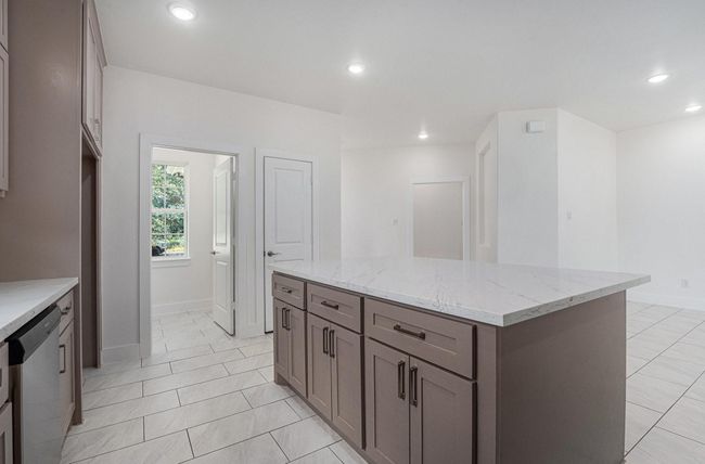 This modern kitchen features a large marble-topped island with ample cabinetry, sleek tile flooring, and plenty of natural light from a nearby window. | Image 14