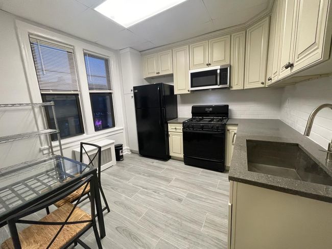 Kitchen with black appliances, a sink, dark stone countertops, tasteful backsplash, and cream cabinets | Image 4