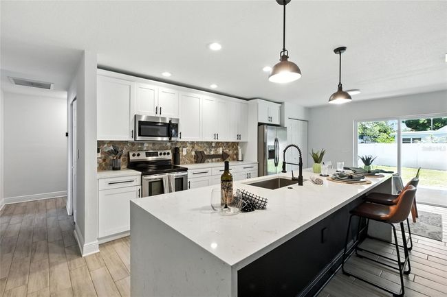 Generous cabinet storage and expansive prep space define this kitchen, featuring a striking waterfall-edge quartz island, full pantry, and modern stainless steel appliances. The sleek tile backsplash adds just the right texture and tone. | Image 13