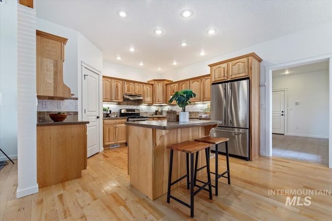 Kitchen featuring appliances with stainless steel finishes, a kitchen bar, a center island, light wood-style flooring, and backsplash | Image 18
