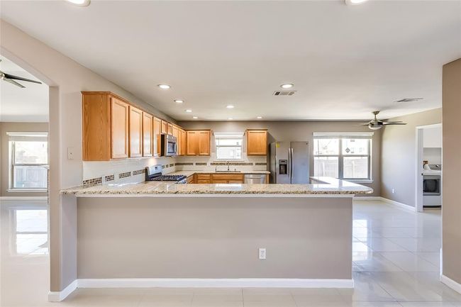Kitchen with appliances with stainless steel finishes, a ceiling fan, light stone counters, a peninsula, and backsplash | Image 10
