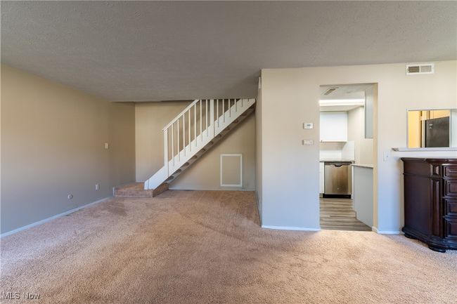 Unfurnished living room featuring carpet flooring, a textured ceiling, visible vents, baseboards, and stairs | Image 6