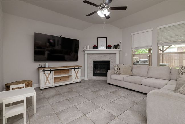 Living room featuring ceiling fan, light ceramic tile floors, a gas log fireplace, vaulted ceiling, large windows with coverings, and baseboards | Image 4