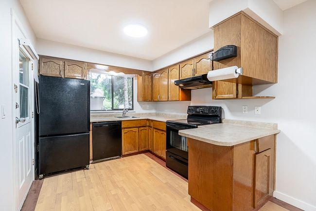 Kitchen featuring black appliances, under cabinet range hood, light countertops, light wood-style floors, and brown cabinetry | Image 8