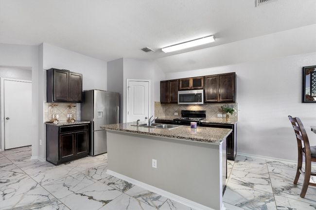 Kitchen featuring appliances with stainless steel finishes, light marble finish floors, a sink, dark brown cabinets, and vaulted ceiling | Image 8