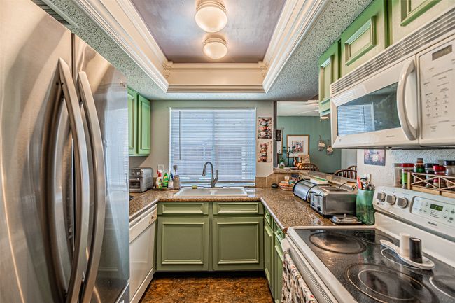 Kitchen with green cabinetry, white appliances, a sink, a raised ceiling, and crown molding | Image 9
