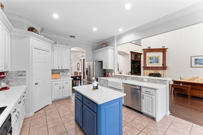 Kitchen with appliances with stainless steel finishes, blue cabinets, arched walkways, white cabinets, and light countertops | Image 10