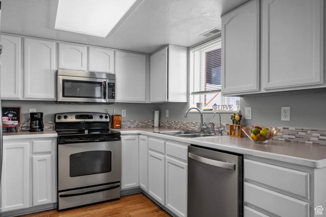Kitchen with appliances with stainless steel finishes, white cabinetry, light countertops, and light wood finished floors | Image 9
