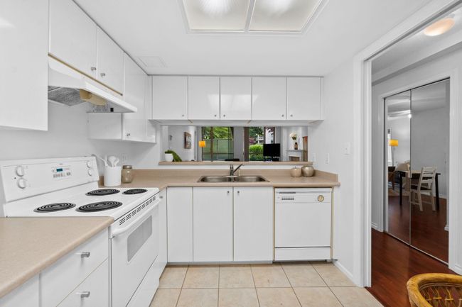Kitchen featuring white appliances, under cabinet range hood, a sink, light countertops, and white cabinetry | Image 9