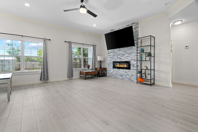Living area with crown molding, a ceiling fan, a stone fireplace, wood finished floors, and recessed lighting | Image 7