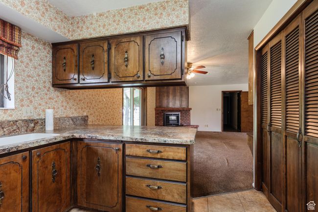Kitchen with a peninsula, ceiling fan, wallpapered walls, open floor plan, and a fireplace | Image 9