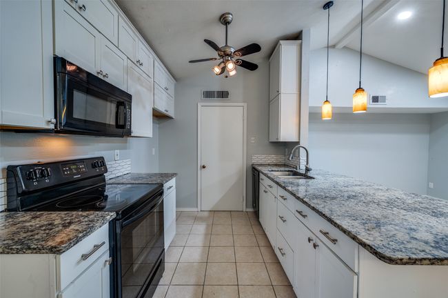 Kitchen with black appliances, a peninsula, ceiling fan, and dark stone countertops | Image 10