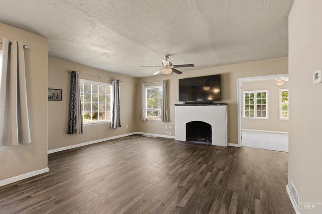 Unfurnished living room featuring a textured ceiling, a fireplace with flush hearth, dark wood-style floors, and a ceiling fan | Image 7