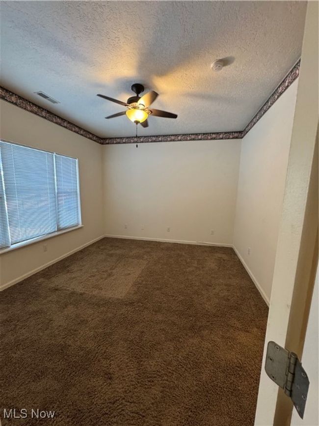 Unfurnished room with ceiling fan, dark carpet, and a textured ceiling | Image 22