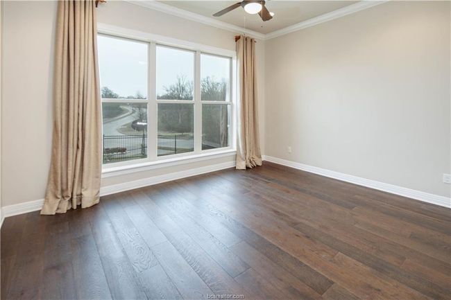 Empty room with baseboards, a ceiling fan, dark wood-type flooring, and crown molding | Image 23
