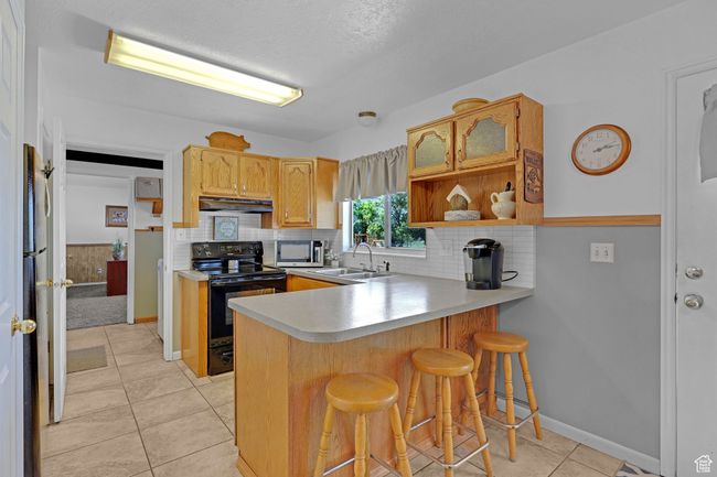 Kitchen with electric range, under cabinet range hood, a sink, a peninsula, and open shelves | Image 9