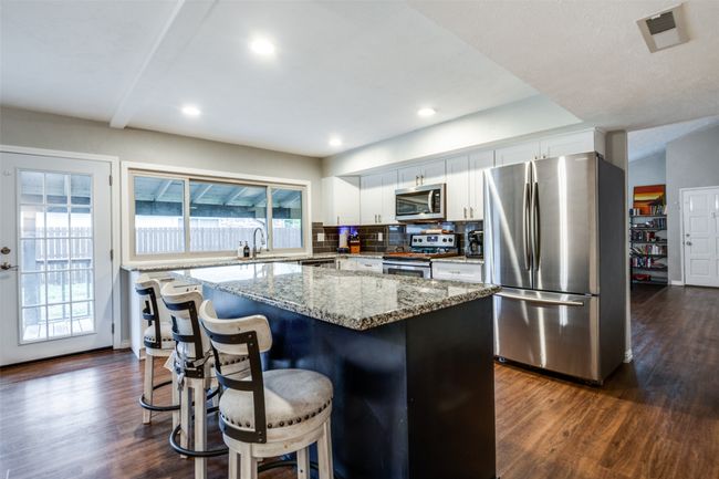 Kitchen featuring tasteful backsplash, dark wood-style flooring, a center island, and appliances with stainless steel finishes | Image 7