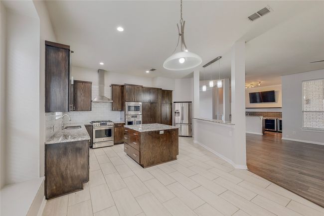 Kitchen featuring appliances with stainless steel finishes, a sink, wall chimney exhaust hood, dark brown cabinetry, and decorative backsplash | Image 15