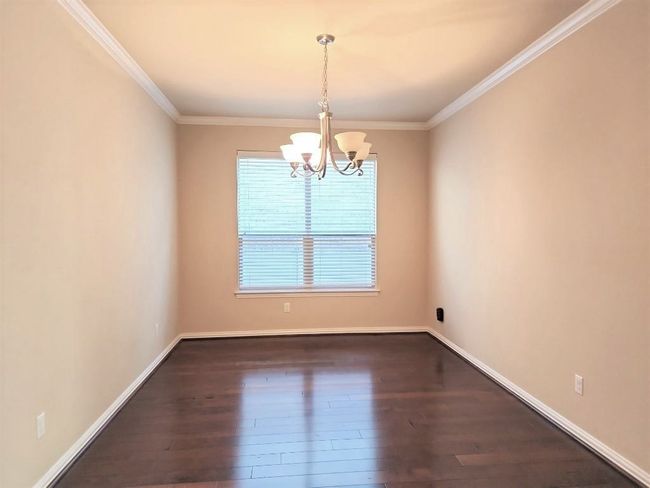 Empty room featuring a chandelier, crown molding, dark wood-type flooring, and baseboards | Image 4