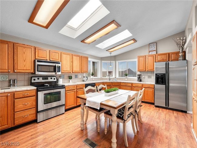 Kitchen with visible vents, lofted ceiling with skylight, decorative backsplash, appliances with stainless steel finishes, and light wood-style floors | Image 22