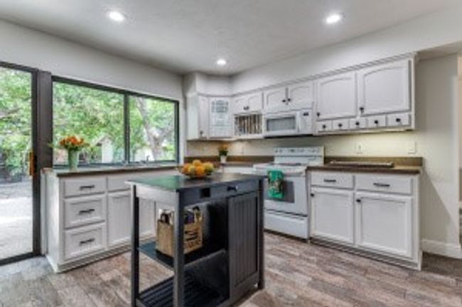 Kitchen featuring white cabinets, dark countertops, wood finished floors, and white appliances | Image 12