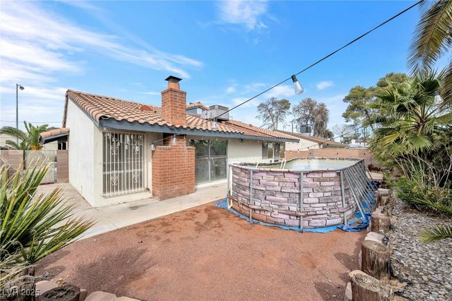 Rear view of property featuring a tile roof, fence, a fenced in pool, and a chimney | Image 25
