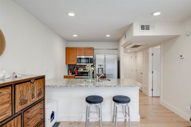 Kitchen with appliances with stainless steel finishes, light wood-type flooring, decorative backsplash, a breakfast bar area, and recessed lighting | Image 10