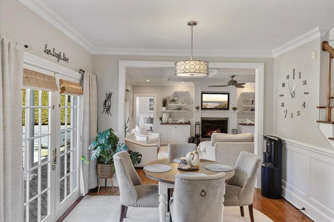 Dining area with a warm lit fireplace, a wainscoted wall, light wood finished floors, ceiling fan, and ornamental molding | Image 12