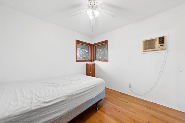 Bedroom with baseboards, a wall mounted air conditioner, ceiling fan, and wood finished floors | Image 10