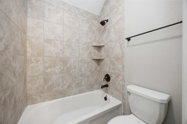 This bathroom features a classic bathtub with beige tile surround, built-in corner shelves, and dark bronze fixtures. A white toilet is adjacent, complemented by a simple towel bar. | Image 34
