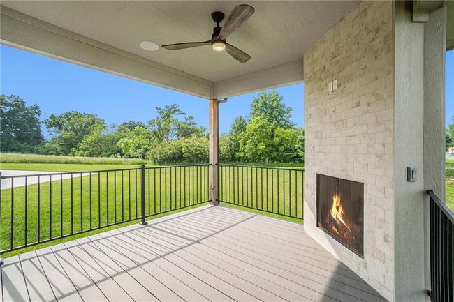 Deck with a fireplace, a ceiling fan, a yard, and view of scattered trees | Image 63