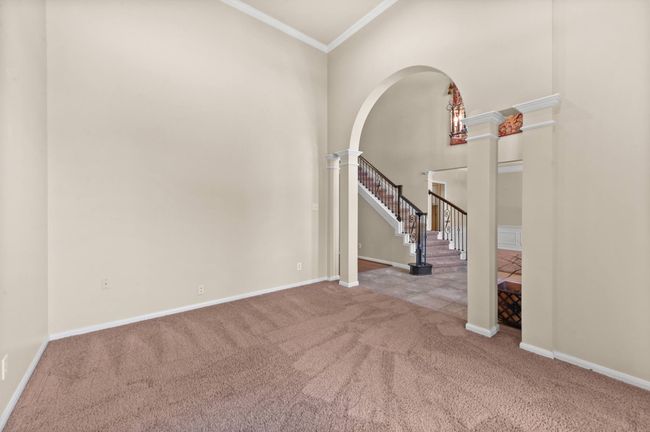 Carpeted empty room featuring decorative columns, arched walkways, ornamental molding, stairway, and a towering ceiling | Image 5