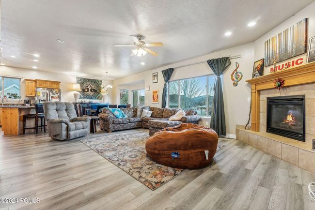 Living room with ceiling fan with notable chandelier, light hardwood / wood-style floors, a textured ceiling, and a tile fireplace | Image 5