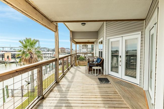 This photo shows a spacious wooden deck with a waterfront view, featuring two wicker chairs and a small table and offers access through elegant French doors, perfect for relaxing and enjoying the serene surroundings. | Image 32
