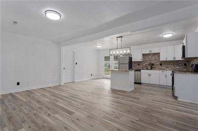 Kitchen featuring light wood-type flooring, appliances with stainless steel finishes, white cabinetry, a kitchen island, and tasteful backsplash | Image 3