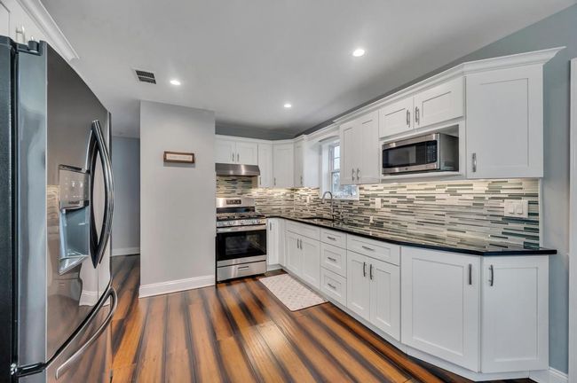 Kitchen featuring a sink, appliances with stainless steel finishes, dark countertops, under cabinet range hood, and visible vents | Image 5