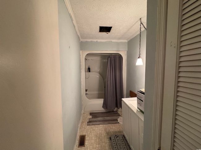 Bathroom featuring a textured ceiling, vanity, shower / bathtub combination with curtain, and ornamental molding | Image 12