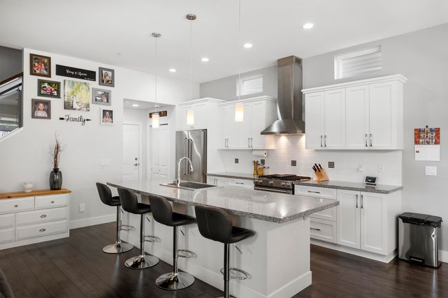 Kitchen featuring a sink, dark wood-type flooring, appliances with stainless steel finishes, white cabinetry, and wall chimney exhaust hood | Image 10