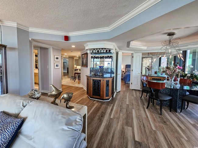 Interior space with a textured ceiling, wood finished floors, a notable chandelier, ornamental molding, and a tray ceiling | Image 8