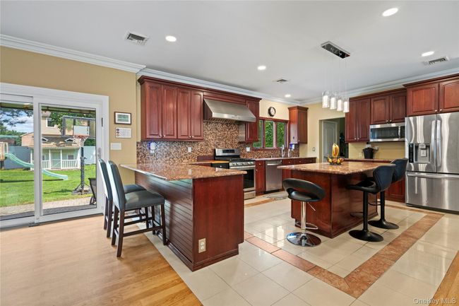 Kitchen with a breakfast bar area, light stone countertops, crown molding, stainless steel appliances, and a center island | Image 7