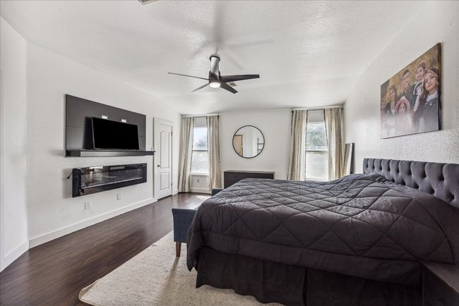 Bedroom featuring wood finished floors, a textured ceiling, a glass covered fireplace, ceiling fan, and baseboards | Image 16