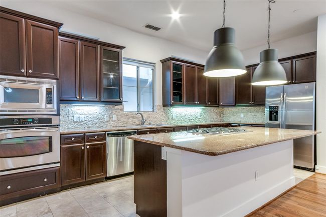 Kitchen featuring visible vents, tasteful backsplash, dark brown cabinets, light stone counters, and stainless steel appliances | Image 10